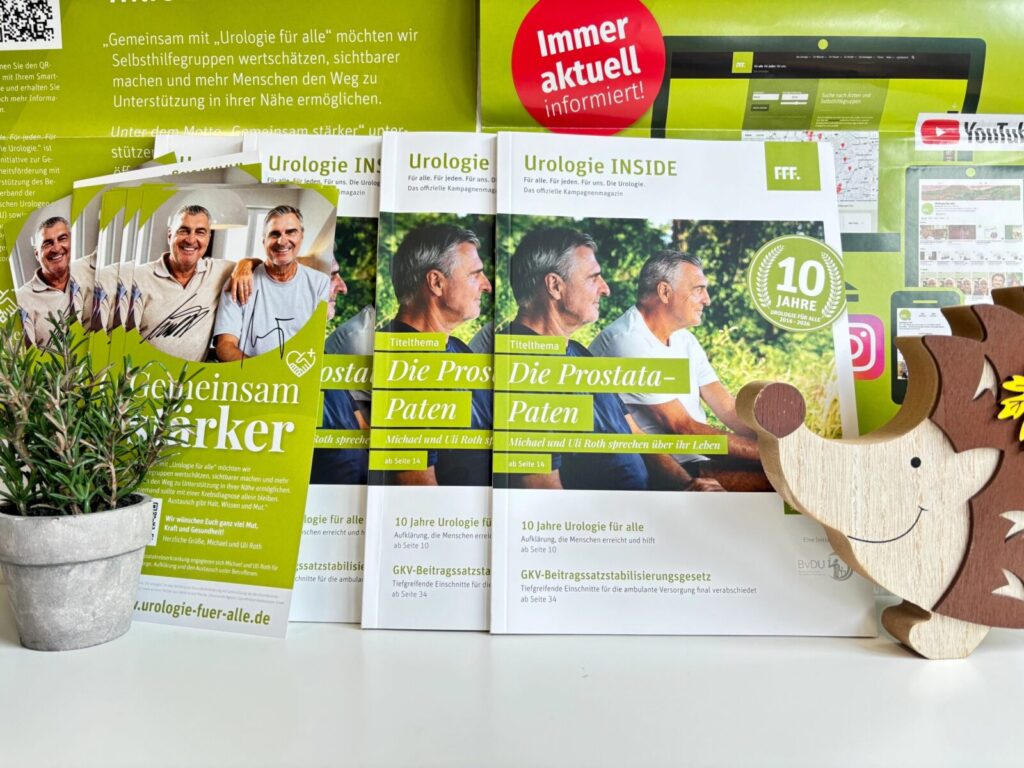 Mehrere Broschüren zum Thema Urologie/Prostata auf einem Tisch, links eine kleine Topfpflanze, rechts ein hölzernes Nashorn-Spielzeug.